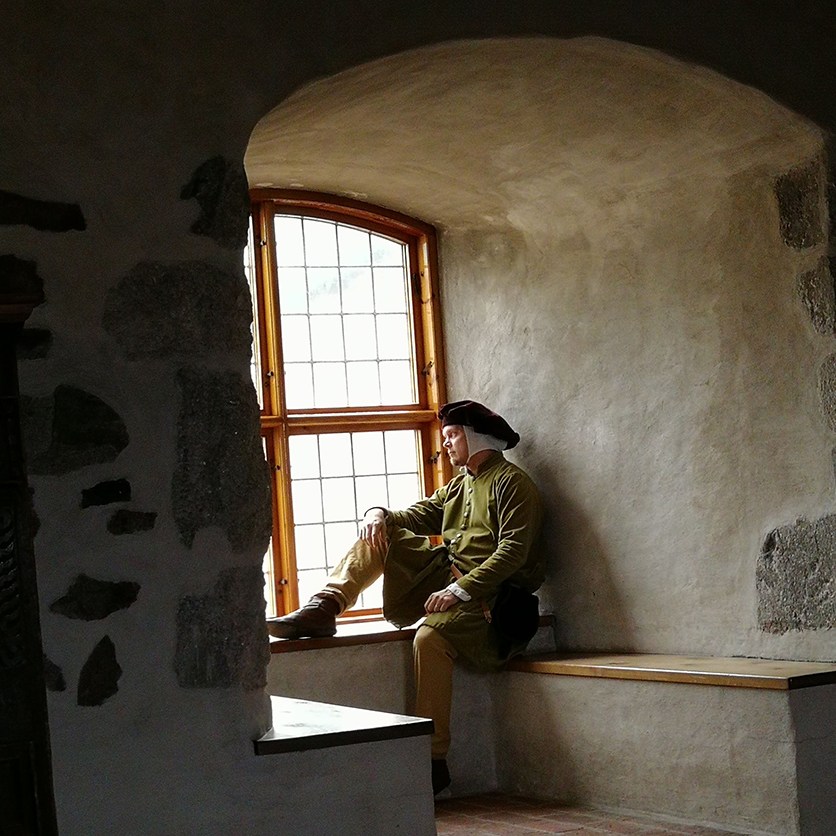 Keskiaikavaatteisiin pukeunut miesoletettu istuu Turun linnan ikkunasyvennyksessä