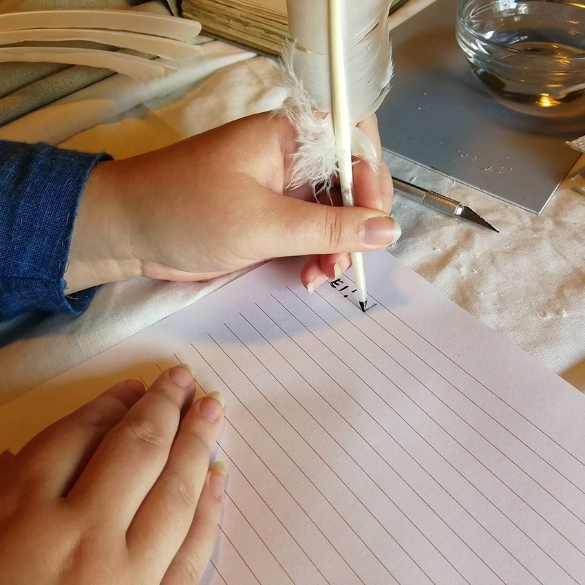 Vasenkätinen henkilö kirjoittaa sulkakynällä ja musteella