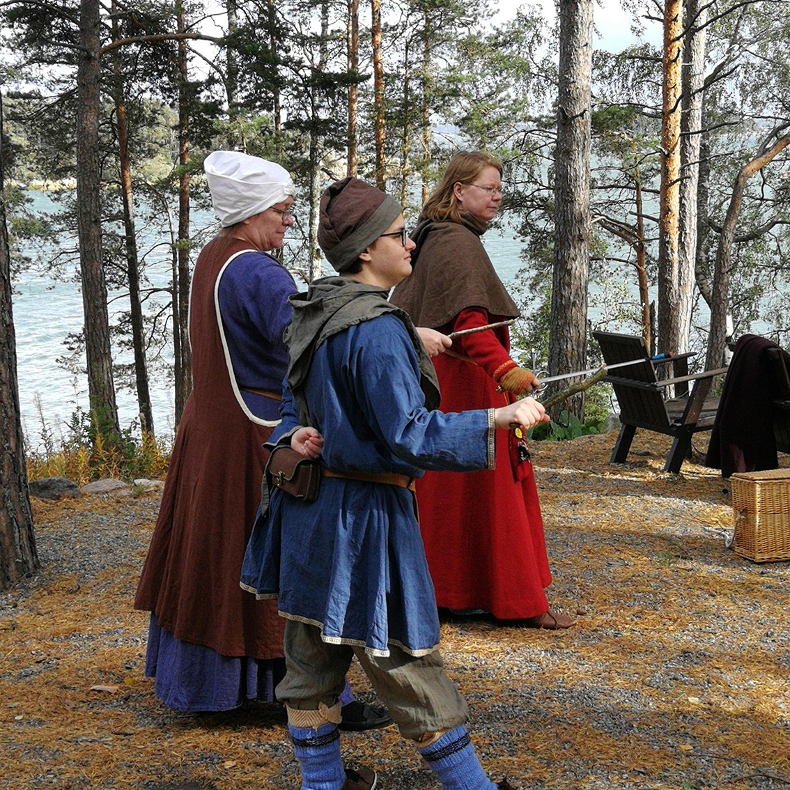 Kolme keskiaikaisiin vaatteisiin puettua harrastajaa harjoittelee miekkailun alkeita