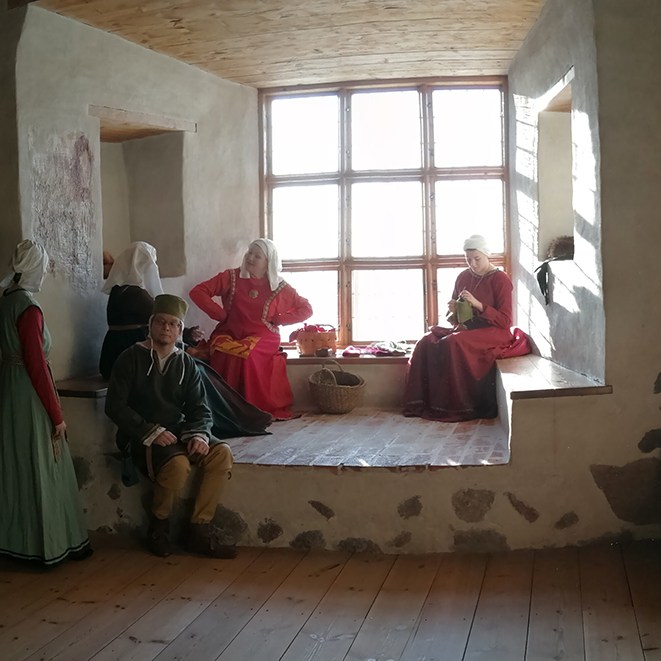 Keskiaikaisiin vaattesiin pukeutuneita harrastajia Turun linnan Rouvainhuoneen ikkunasyvennyksessä