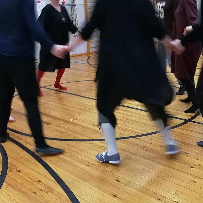 Käsikädessä piirissä laukkaavia tanssijoita liikuntasalissa